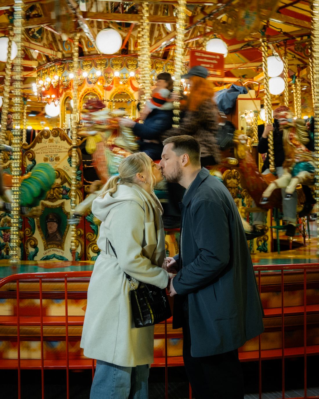 Couple kissing in front of a spinning carousel