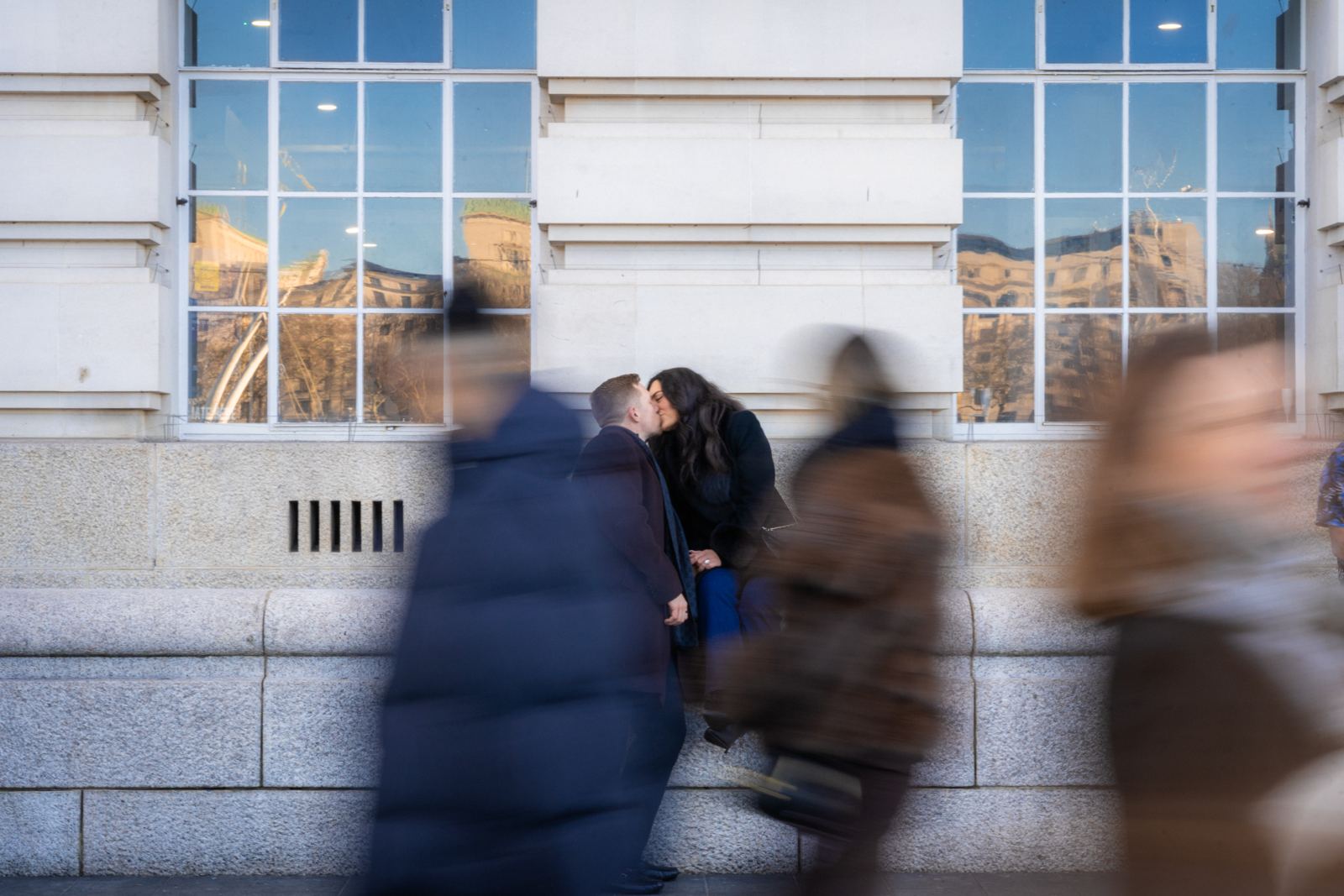 Couple kissing against a wall while blurred crowds walk past