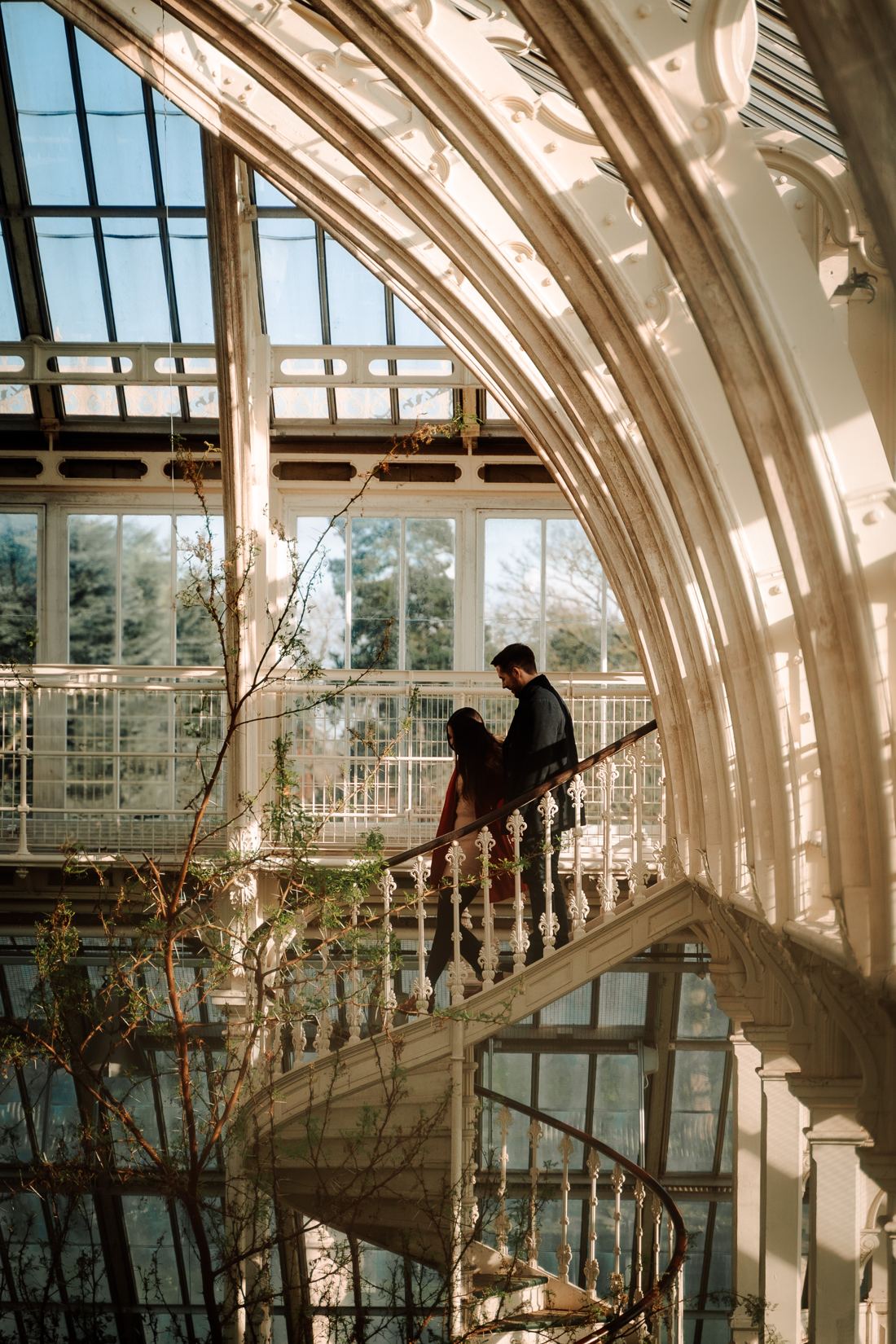 Couple on a white spiral staircase inside a Victorian glasshouse