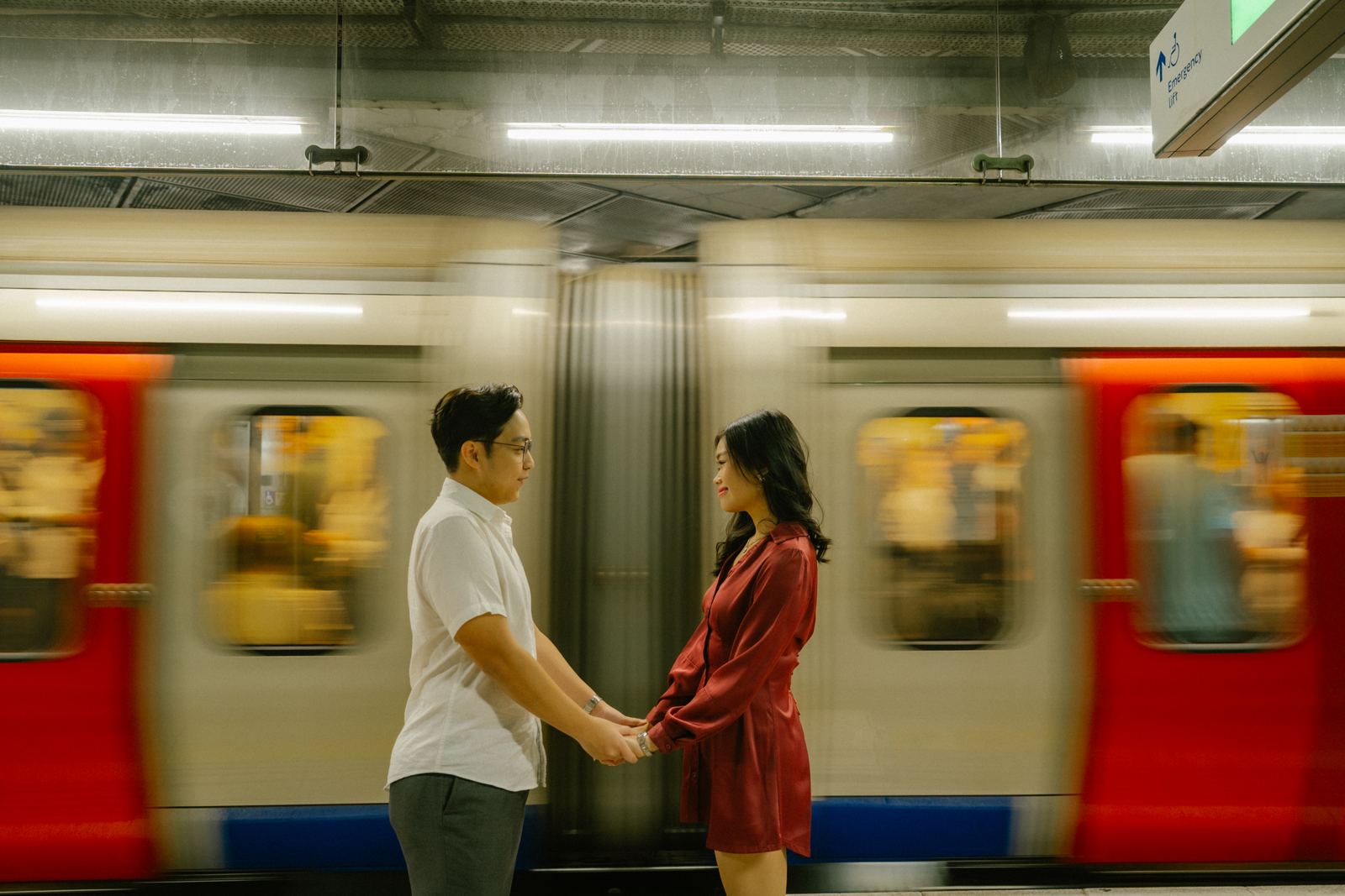 Couple holding hands on a Tube platform as a train rushes past