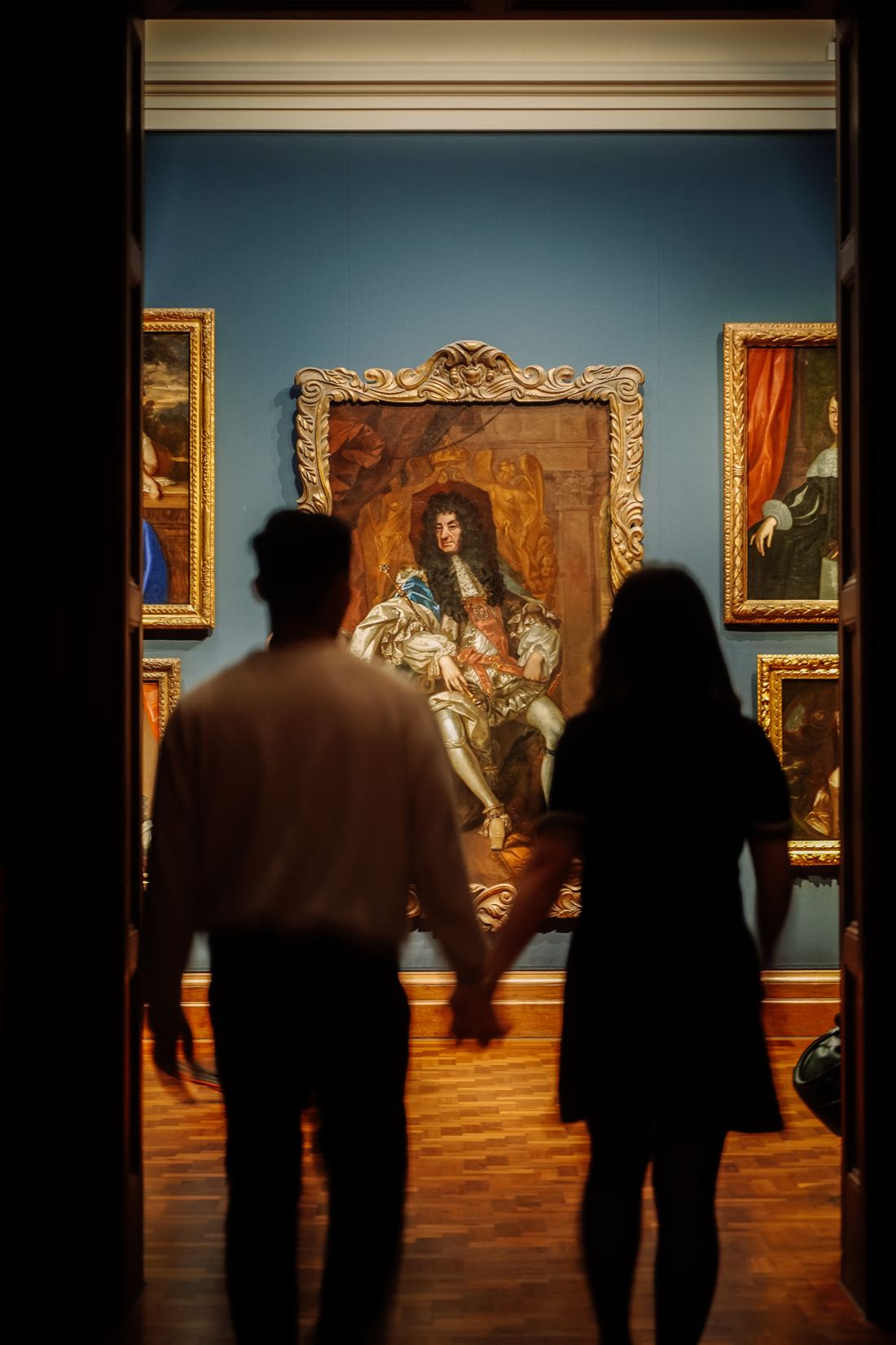 Couple walking hand in hand into a gallery of old paintings